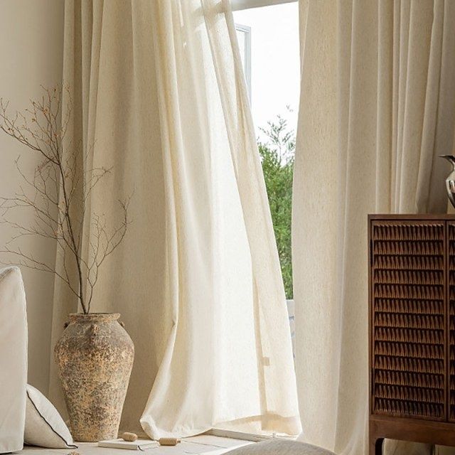 Tunga beige gardiner vid ett fönster i ett ljust vardagsrum
