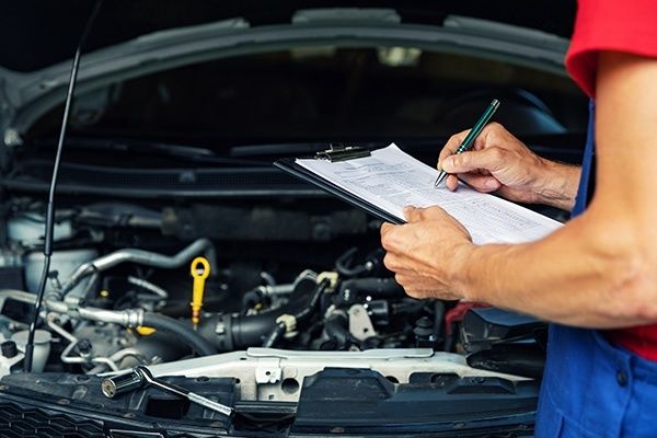 Person kontrollerar bilens motor med checklista inför ett möjligt köp